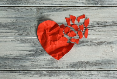 Crumpled red paper heart with torn away pieces on wooden background, top view