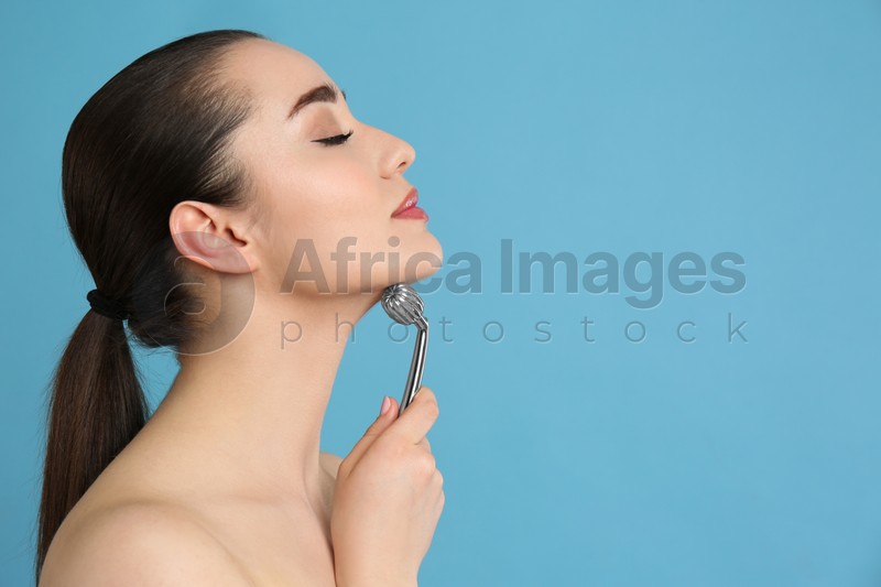 Woman using metal face roller on light grey  background, space for text