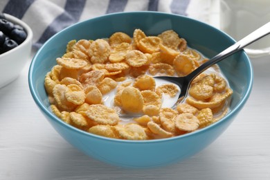 Bowl of tasty corn flakes served for breakfast on white wooden table, closeup