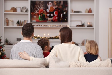 Photo of Family watching Christmas movie via TV in cosy room, back view. Winter holidays atmosphere