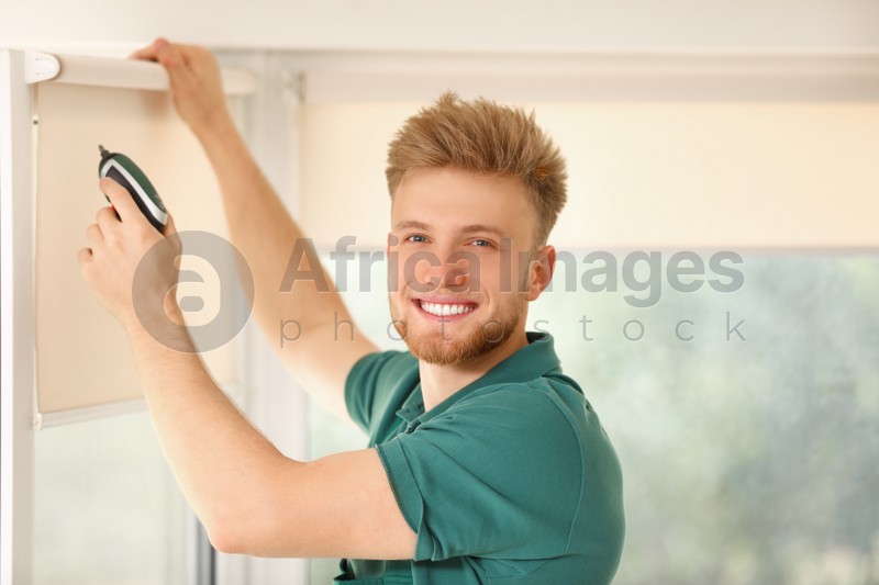 Image of Handyman with cordless screwdriver installing roller window blind indoors