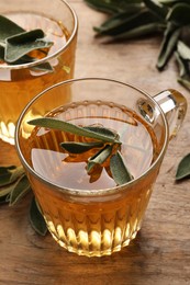 Cups of aromatic sage tea with fresh leaves on wooden table, closeup