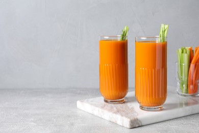 Photo of Glasses of tasty carrot juice with celery sticks on light grey table, space for text