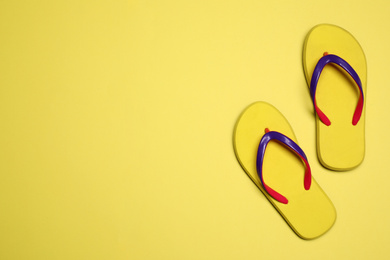 Flip flops on yellow background, top view with space for text. Beach objects