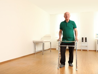 Elderly man using walking frame indoors. Space for text