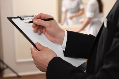 Photo of Man wearing suit with clipboard checking maid's work in hotel room, closeup. Professional butler courses
