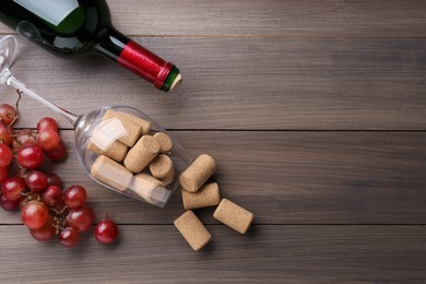 Photo of Bottle of wine, glass with corks and grapes on wooden table, flat lay. Space for text
