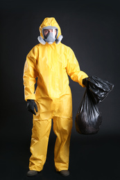Man in chemical protective suit holding trash bag on black background. Virus research