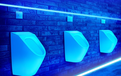 Ceramic urinals in men's public restroom lit with UV blue light