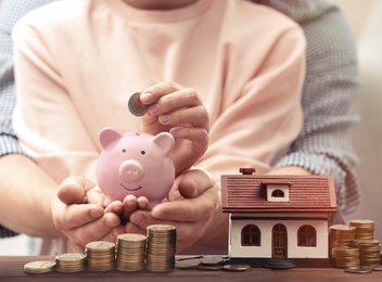 Couple putting money into piggy bank for future house purchase, closeup