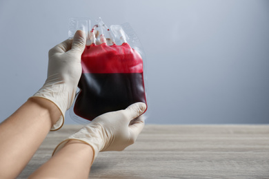 Woman holding blood for transfusion at wooden table, closeup with space for text. Donation concept