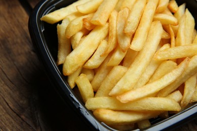Container with French fries on wooden table, closeup. Food delivery service