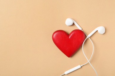 Modern earphones and red heart on beige background, flat lay with space for text. Listening love music songs