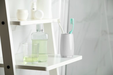 Bottle and glass with mouthwash on white shelf indoors, space for text