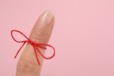 Woman showing index finger with tied red bow as reminder on pink background, closeup, Space for text