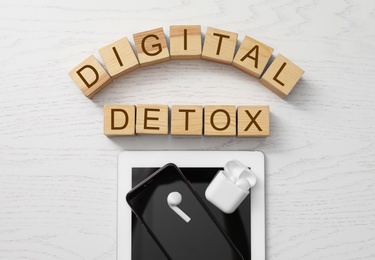Different gadgets and cubes with words DIGITAL DETOX on white wooden background, flat lay