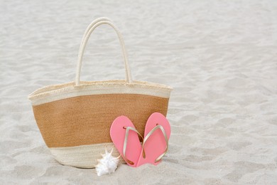 Stylish straw bag, flip flops and seashell on sand outdoors, space for text. Beach accessories