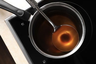 Photo of Saucepan and ladle with used cooking oil on stove, top view