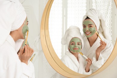 Young mother and her daughter with facial masks near mirror in bathroom