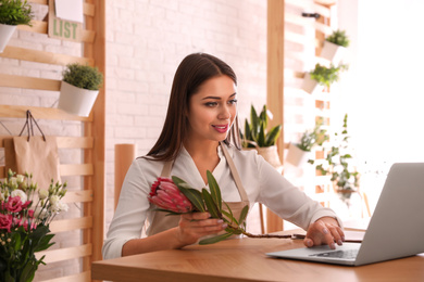 Photo of Florist with protea flower working on laptop in store