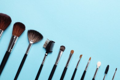 Set of makeup brushes on light blue background, flat lay. Space for text