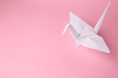 Photo of Origami art. Handmade paper crane on pink background, above view. Space for text