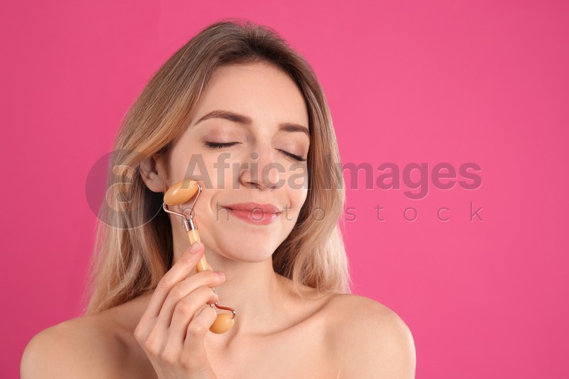 Photo of Young woman using natural jade face roller on pink background