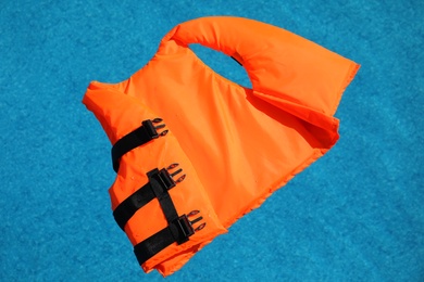 Bright orange life jacket floating in swimming pool, top view