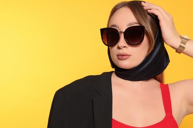 Young woman with lip piercing and sunglasses on yellow background. Space for text
