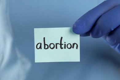 Doctor holding paper card with word ABORTION, closeup