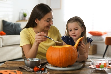 Mother and daughter making pumpkin jack o'lantern at table indoors. Halloween celebration