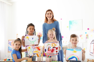 Cute little children with teacher showing their paintings at lesson indoors