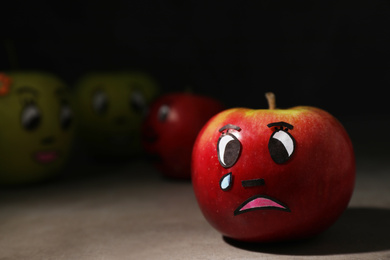 Apple with crying face on grey table, closeup. Concept of jealousy