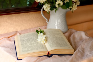 Open book and beautiful jasmine flowers on pink fabric indoors
