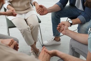 Psychotherapist and group of drug addicted people holding hands together at therapy session, closeup