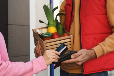 Client paying courier for fresh products with credit card outdoors, closeup. Food delivery service