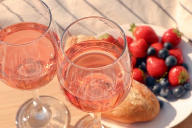 Glasses of delicious rose wine and food on wooden board, closeup