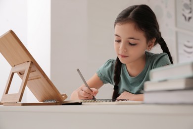 Little girl doing homework with tablet at table in room
