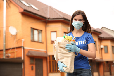 Female volunteer in protective mask and gloves with products on city street. Aid during coronavirus quarantine