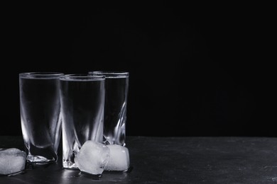 Photo of Vodka in shot glasses with ice on table against black background. Space for text