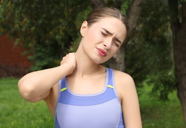 Photo of Young woman suffering from neck pain outdoors