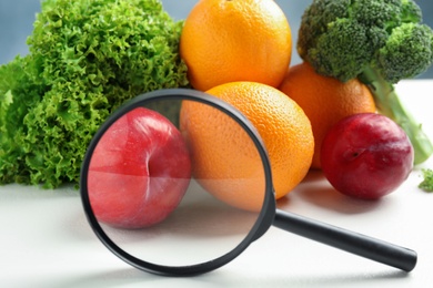 Fresh fruits, vegetables and magnifying glass on white table, closeup. Poison detection
