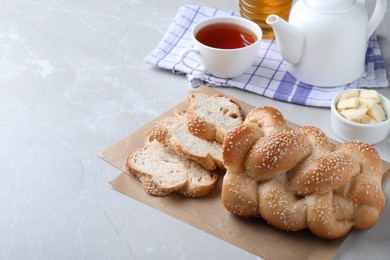 Cut homemade braided bread and freshly brewed tea on light grey table, space for text. Traditional Shabbat challah