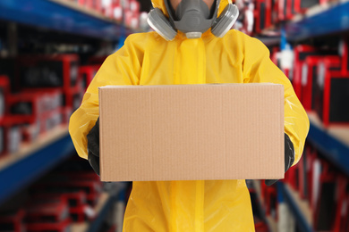 Man wearing chemical protective suit with cardboard box in store, closeup. Wholesale market