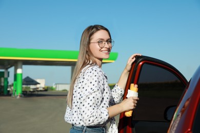 Beautiful young woman with hot dog opening car door at gas station