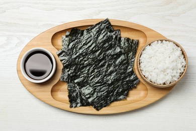Tray with dry nori sheets, rice and soy sauce on white wooden table, top view