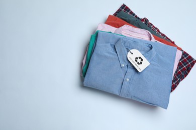 Photo of Stack of clothes with recycling label on light background, top view. Space for text