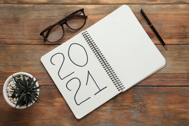 Notebook with number 2021, new year goals. Objects on wooden table, flat lay
