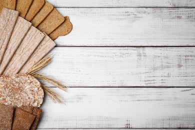 Rye crispbreads, rice cakes and rusks on white wooden table, flat lay