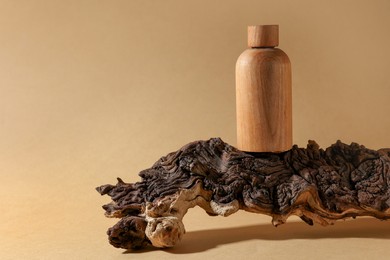 Photo of Wooden bottle of cosmetic product on tree bark against dark beige background, space for text